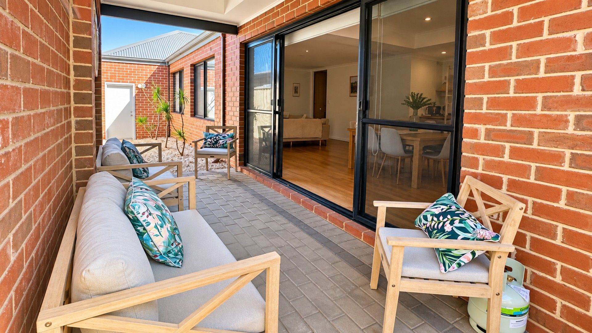 A patio with a sofa and chairs, a sliding glass door leading to a dining area, and a brick wall.