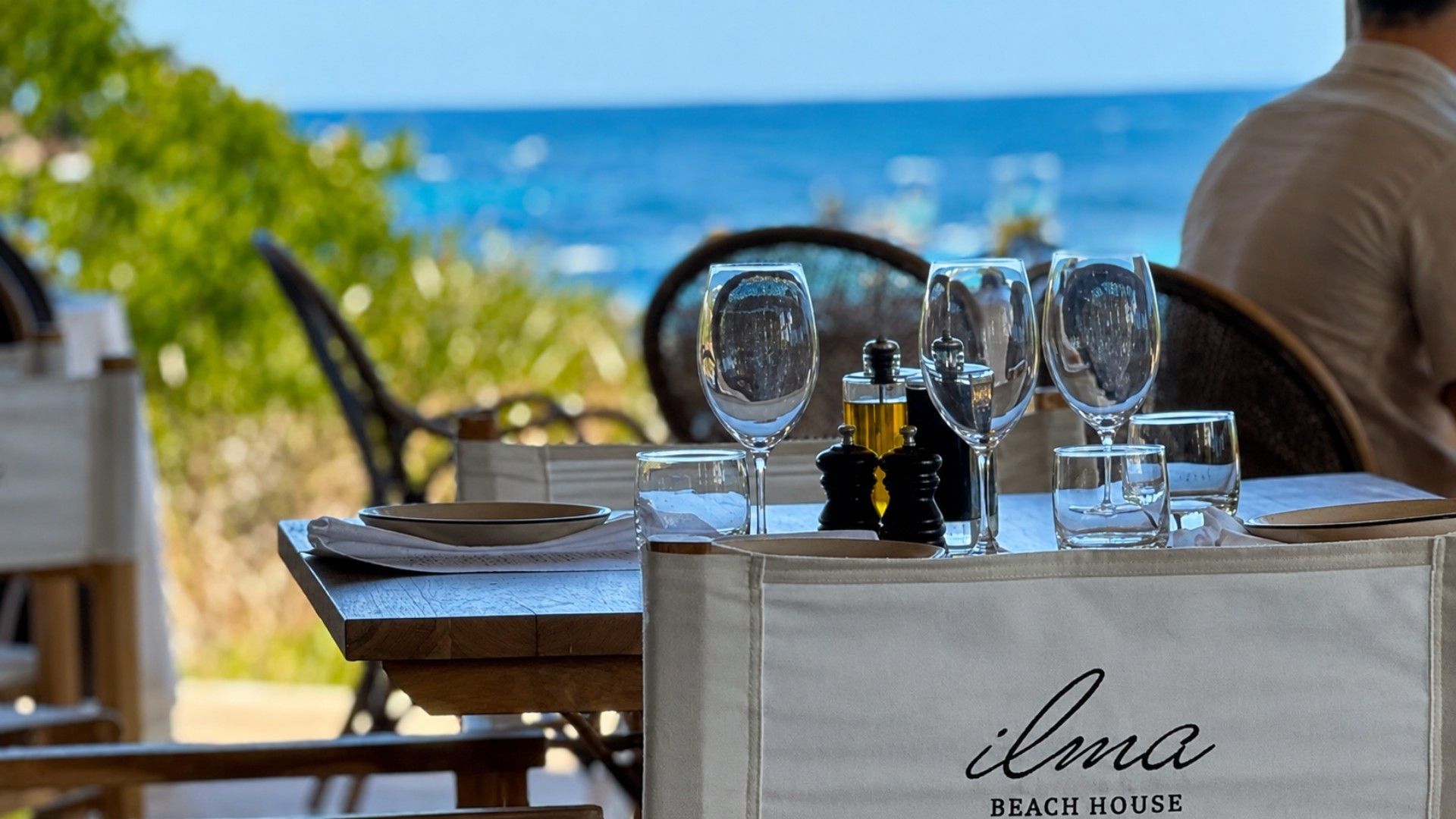 A table set for dining with a view of the ocean, a bottle of olive oil, and a glass of water.