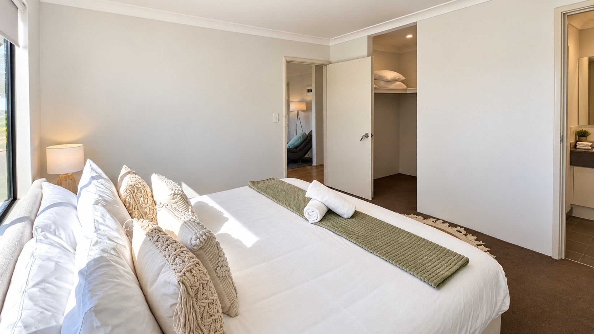 A hotel room with a large bed, a bedside table with a lamp, a walk-in closet, and a view of the outside.