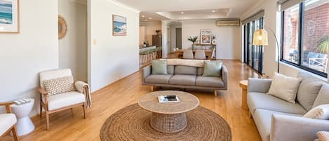 Een moderne woonkamer met een bank, fauteuils, een salontafel en een eethoek op de achtergrond.