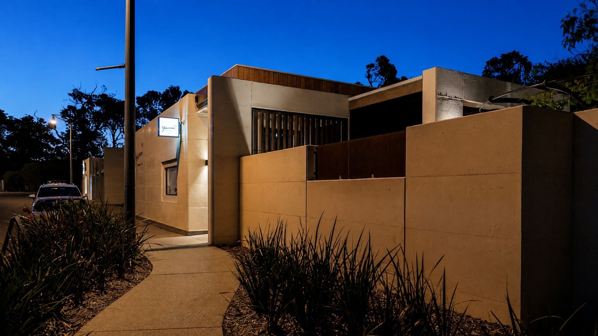 A modern building with a concrete facade, a visible entrance, and a car parked outside.