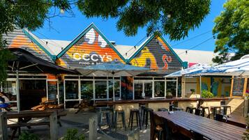 An outdoor seating area with tables and chairs, a covered patio, and a building with a colorful awning.