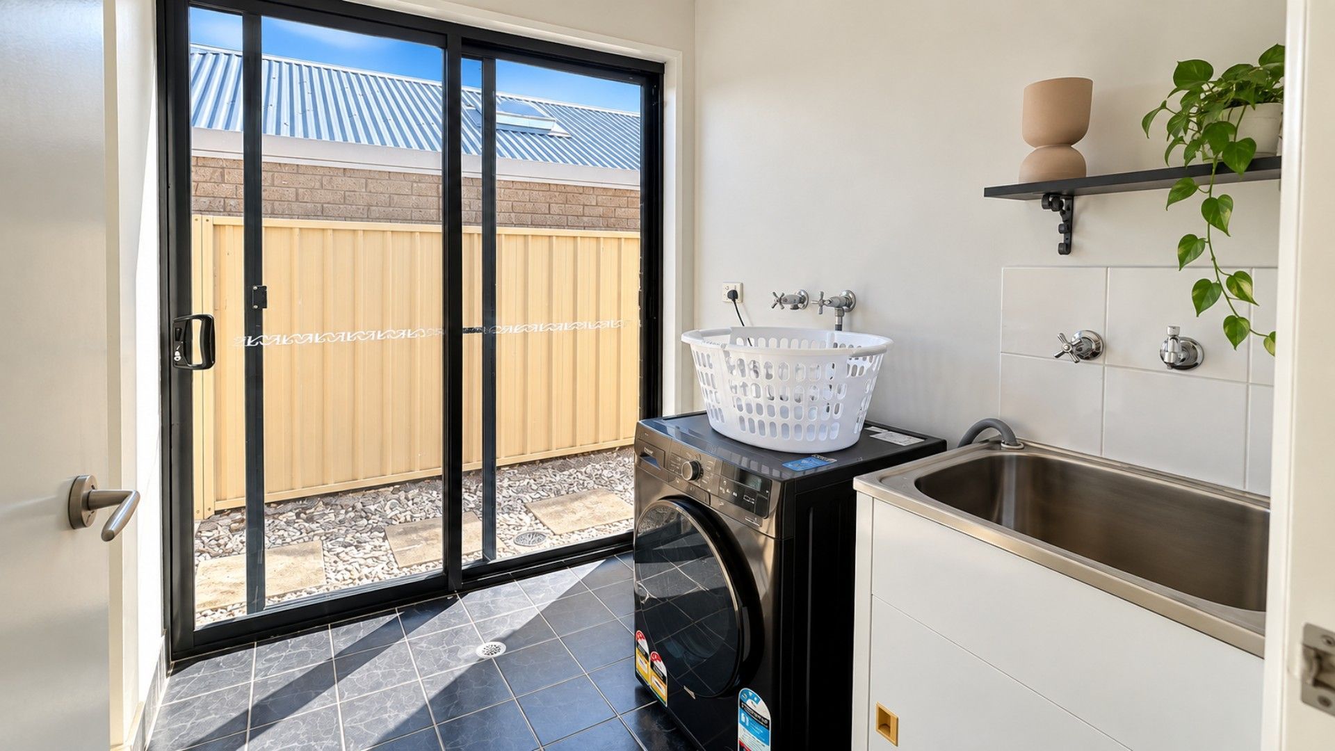 A laundry room with a washing machine, a sink, and a window overlooking a backyard.