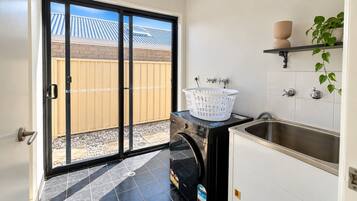 A laundry room with a washing machine, a sink, and a window overlooking a backyard.