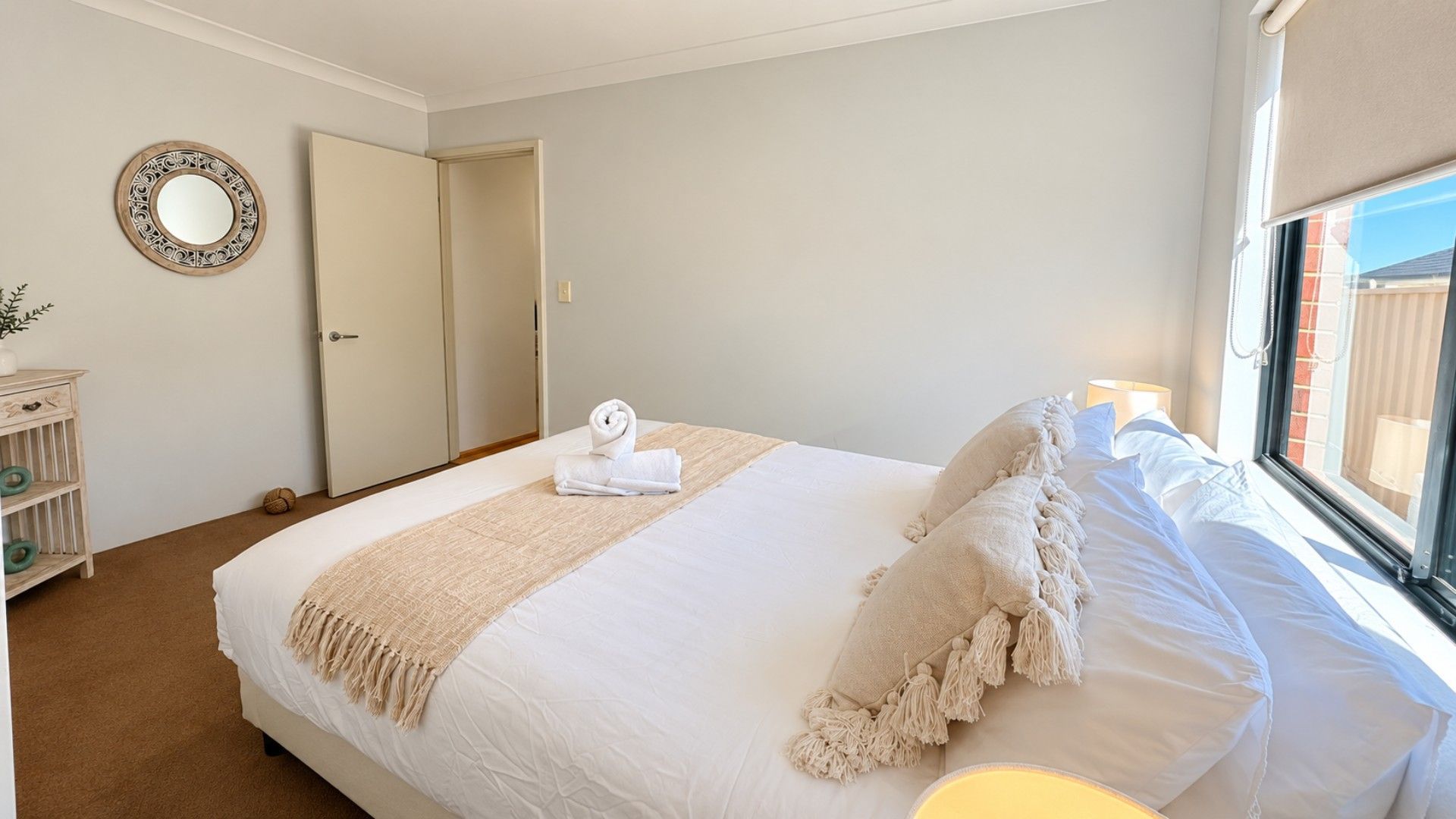 A hotel room with a bed, a bedside table, a mirror, and a window.