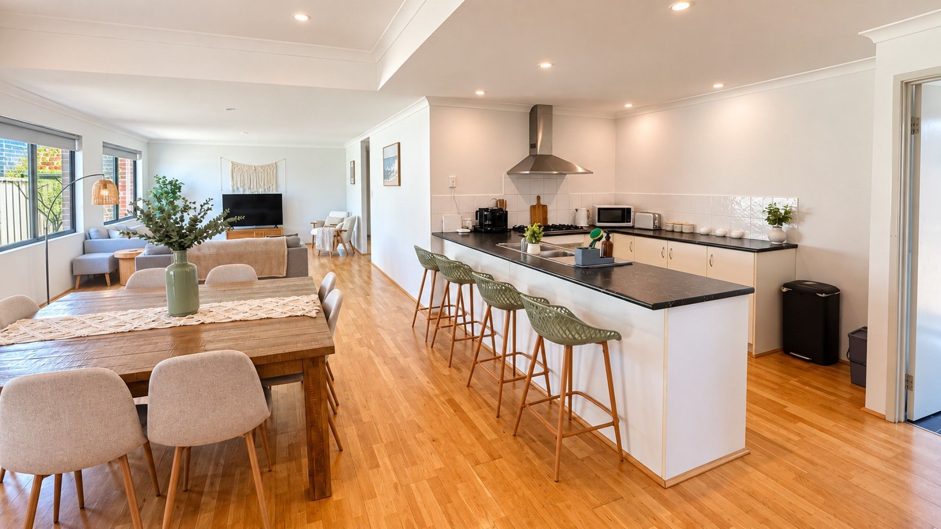 A modern kitchen with a central island, bar stools, and a dining area with a wooden table and chairs.
