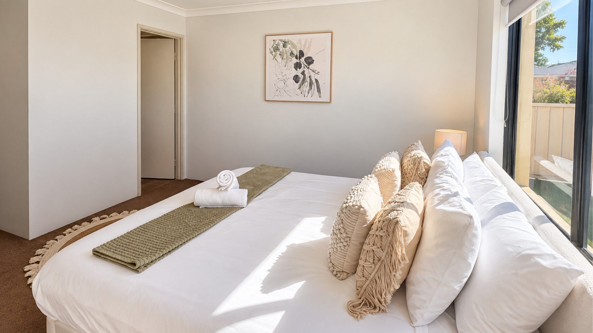 Hotellihuone, jossa on suuri sänky, näkymä ulos ja seinällä kehystetty kasvitieteellinen kuva.