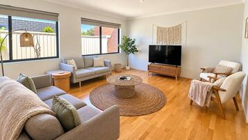 A modern living room with a sofa, armchairs, a coffee table, a TV, and a large window.