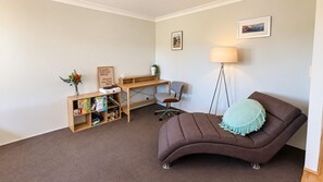 Une pièce avec un canapé marron, un bureau avec une chaise, une bibliothèque, un lampadaire et deux tableaux encadrés accrochés au mur.