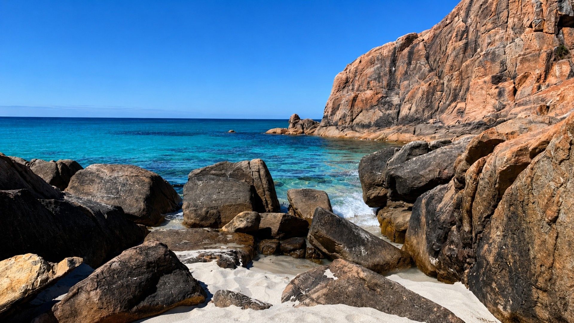 A rocky coastline with clear blue sea and white sand.