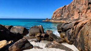 Una costa rocosa con mar azul turquesa y arena blanca.