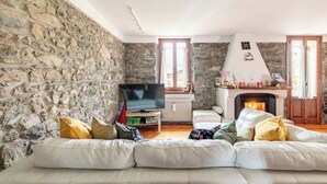 Un salon chaleureux avec un mur en pierre, une cheminée, un téléviseur et un canapé.