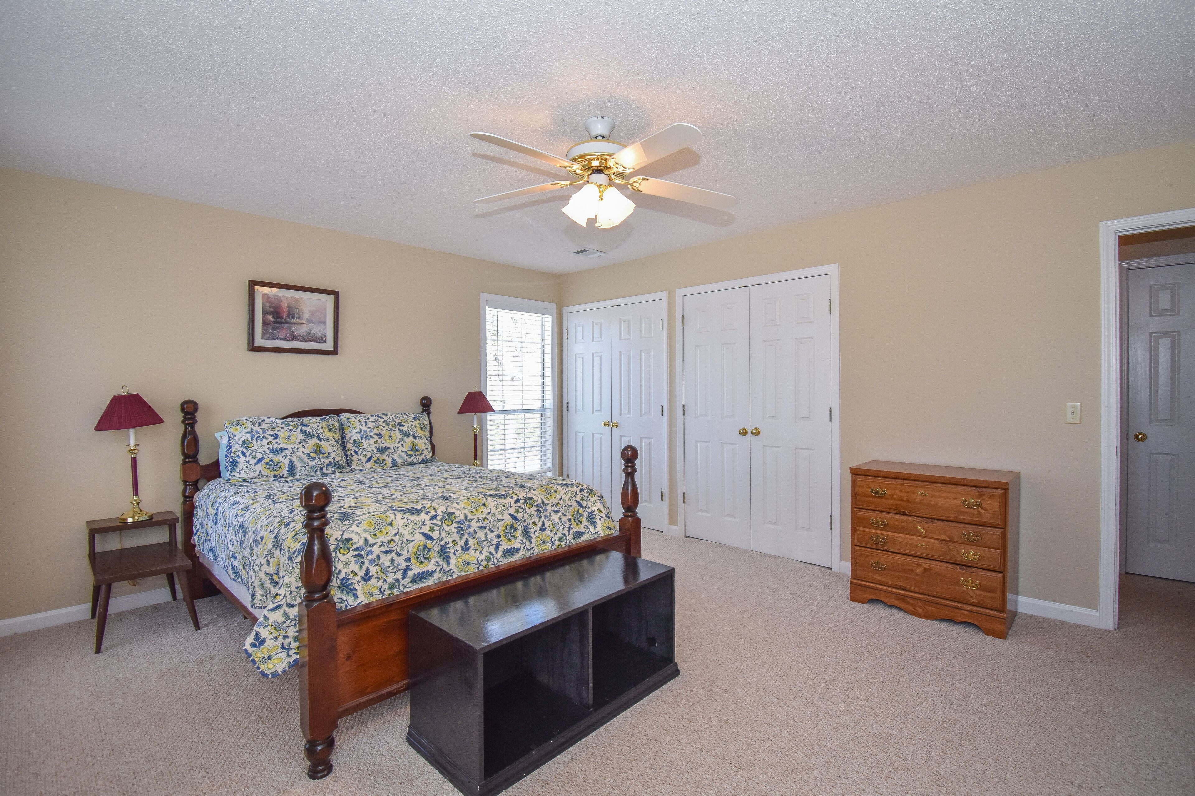 A bedroom with a bed, a dresser, a nightstand, a ceiling fan, and a door.