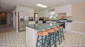 A kitchen with white cabinets, a central island with stools, a refrigerator, and a microwave. - Crystal Clearwaters by Lake Martin Vibe (Dadeville)