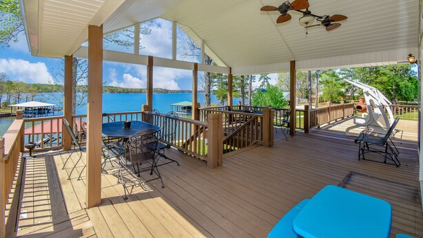 A covered outdoor deck with a table and chairs, a view of the lake, and a wooden railing. - Crystal Clearwaters by Lake Martin Vibe (Dadeville)