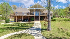 A two-story house with a covered porch, a front entrance, and a driveway leading to a garage. - Crystal Clearwaters by Lake Martin Vibe (Dadeville)