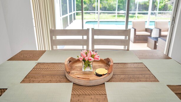 Une table à manger avec un plateau en bois, un vase contenant des fleurs roses et un petit bol.
