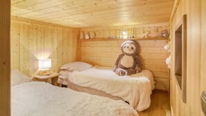 A cozy wooden cabin room with two beds, a nightstand with a lamp, and a teddy bear on the right side. - Le Wood Megève (Megève)