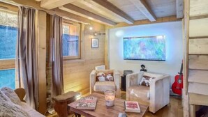 A cozy cabin interior with wooden beams, a television, a guitar, and a fireplace. - Le Wood Megève (Megève)