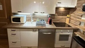 A compact kitchen with white cabinets, a microwave, a sink, and a dishwasher. - Le Wood Megève (Megève)