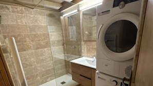 A compact bathroom with a glass shower enclosure, a built-in washing machine, and a small vanity. - Le Wood Megève (Megève)