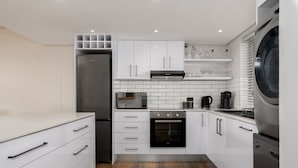 Una cocina moderna con armarios blancos, un refrigerador de acero inoxidable, horno integrado, microondas y lavadora.