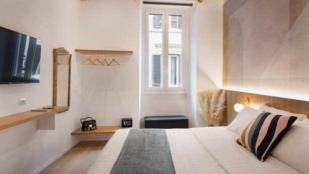 Een moderne slaapkamer met een bed, een televisie, een raam en een nachtkastje.