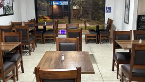 A restaurant with wooden tables and chairs, a glass partition, and a view of the street outside. - Hostal Iñaquito (Quito)