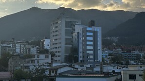 A modern building with multiple floors and a flat roof, surrounded by other residential buildings and mountains in the background. - Hostal Iñaquito (Quito)