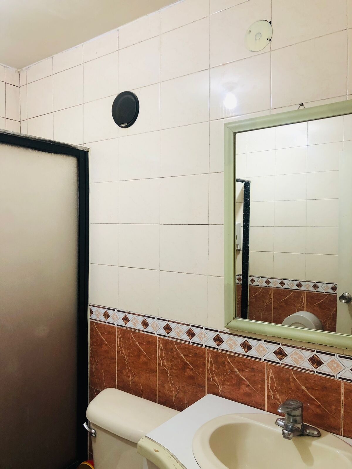 A bathroom with white tiled walls, a brown and white tiled backsplash, a toilet, a sink with a mirror above it, and a black door.