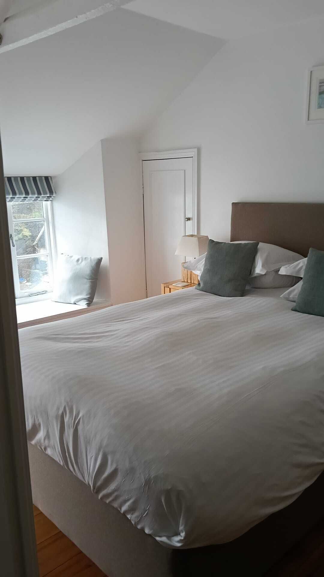 Ein Schlafzimmer mit einem großen Bett, einem Nachttisch mit Lampe, einem Fenster mit Blick und einer Tür.