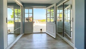Ein Flur mit Holzboden, Glastüren zu einem Außenbereich und ein kleiner Hund, der durch das Glas zu sehen ist.