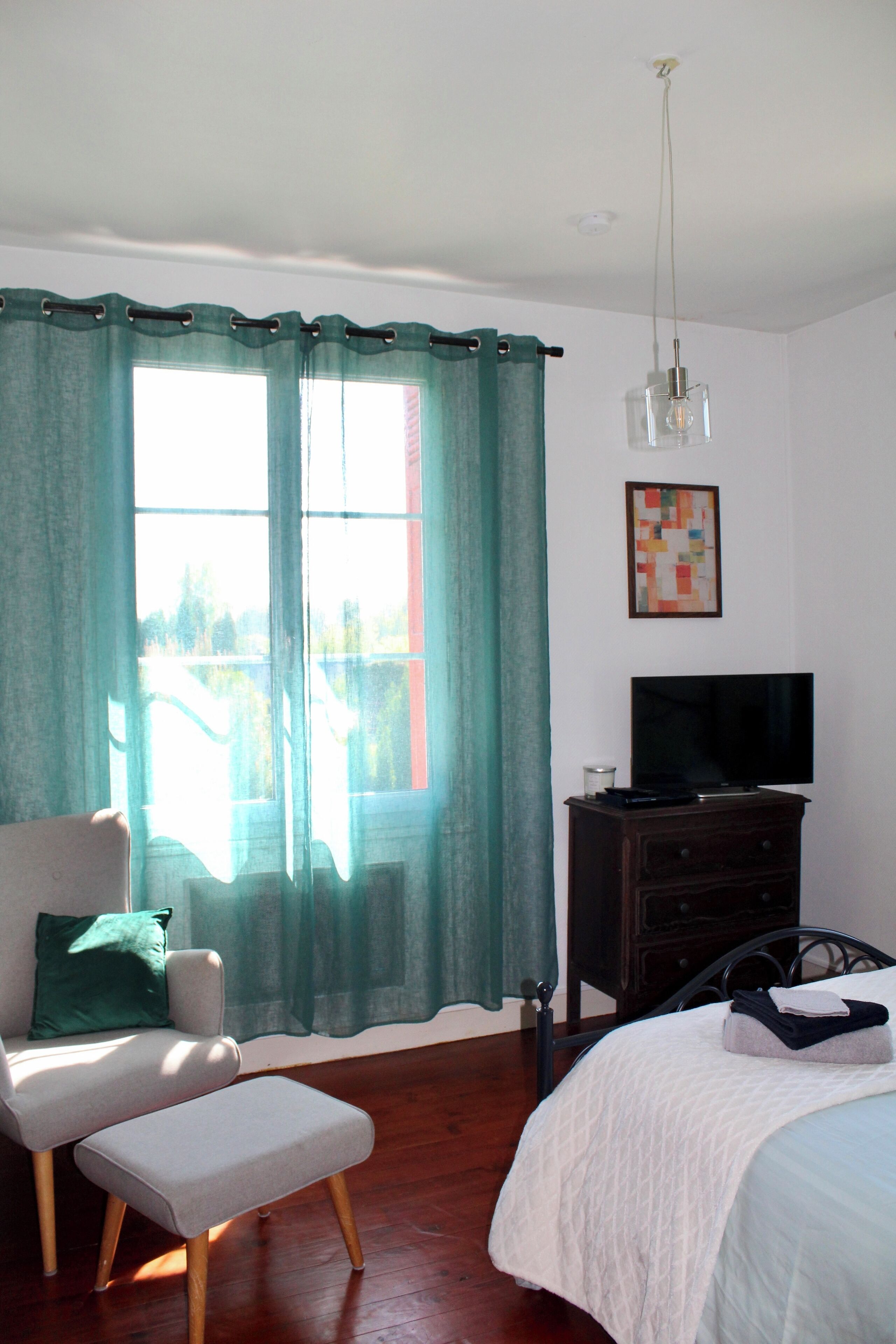 Ein Schlafzimmer mit Bett, Sessel, Schminktisch und Fernseher, mit einem Vorhangfenster.
