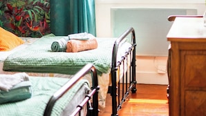 Een slaapkamer met twee bedden, een raam met uitzicht op groen en een radiator.