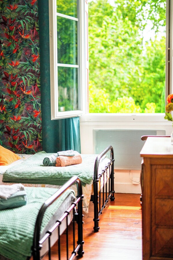 A bedroom with two beds, a window with a view of greenery, and a radiator.