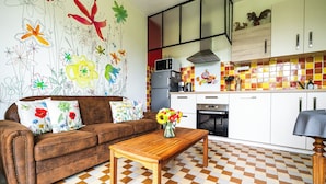 Een woonkamer met een bruine bank, een houten salontafel en een kleurrijke bloemenmuur.