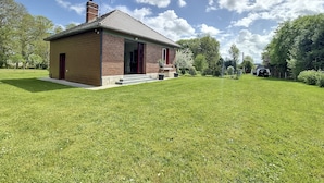 Een tweelaags bakstenen huis met een rode deur en schoorsteen, omgeven door een verzorgd gazon en bomen.