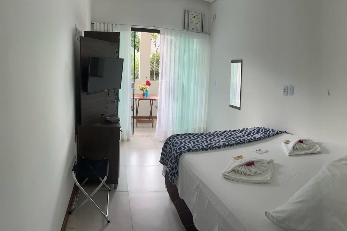A hotel room with a bed, a desk, a TV, and a view of the outside.