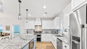 A modern kitchen with white cabinets, granite countertops, stainless steel appliances, and pendant lighting. - Angler's Nook: Stunning Beachfront Home, Private Pool, Pet-Friendly, Sleeps 12 (Indian Pass)