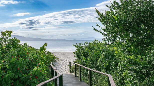 Een houten looppad naar een strand met uitzicht op de zee en verre bergen.