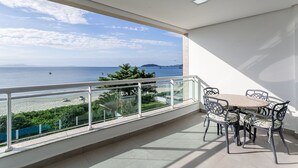 Een balkon met een tafel en stoelen, met uitzicht op een strand en zee.