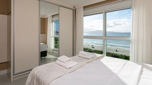 Een slaapkamer met een groot bed, een schuifdeurkast en uitzicht op het strand.