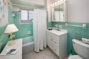 Une salle de bain avec une baignoire, un lavabo, un miroir avec éclairage et une fenêtre avec un rideau.