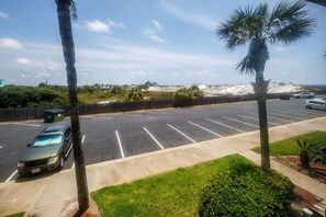 Ein Parkplatz mit einer Reihe geparkter Autos, einer Palme und Blick auf einen Strand mit Dünen im Hintergrund.