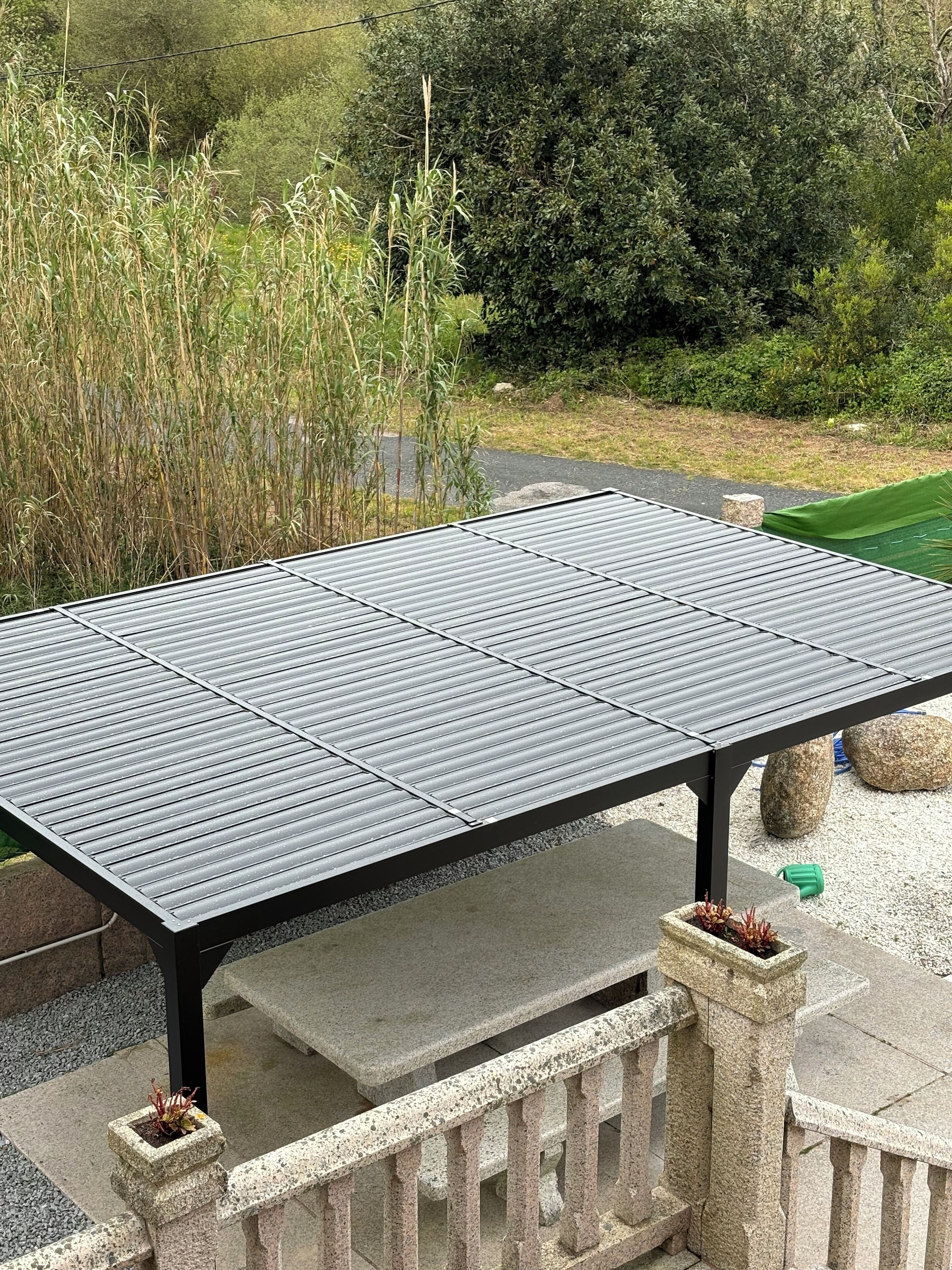 A metal table with a grid pattern, supported by stone pillars, set on a stone patio with a gravel border.