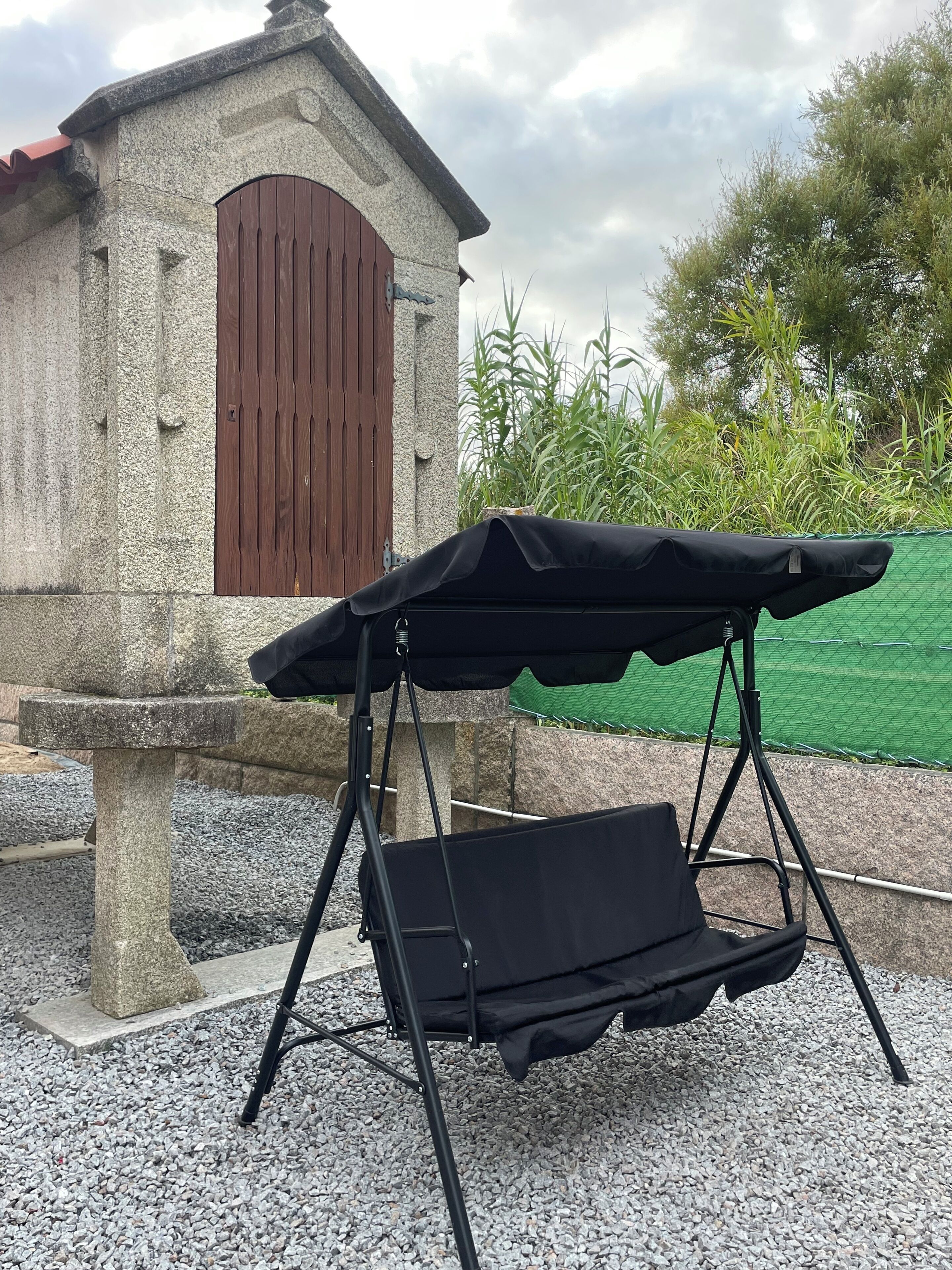 A black outdoor seating area with a swing seat, set against a stone wall with a wooden door.