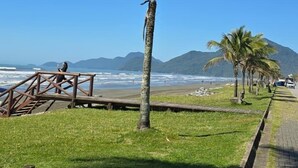 Un paseo marítimo con palmeras, un puente de madera y vistas al océano y las montañas.