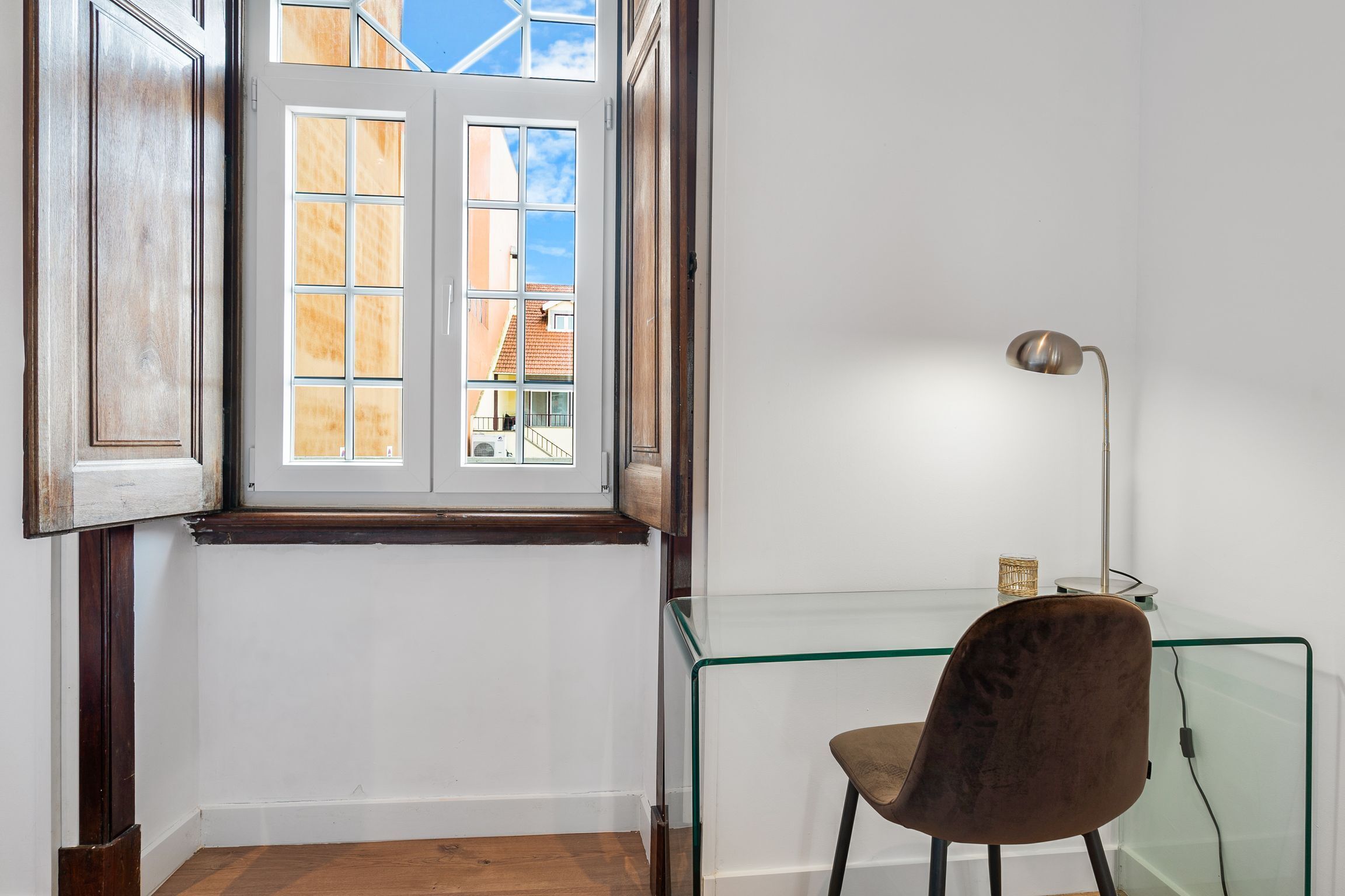 A room with a wooden door, a glass table with a chair, and a floor lamp.