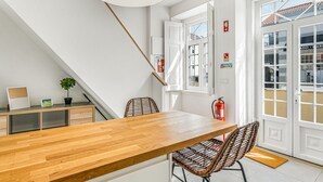 Un comedor moderno con una mesa de madera y sillas de mimbre, una lámpara colgante y vistas al exterior a través de amplios ventanales.