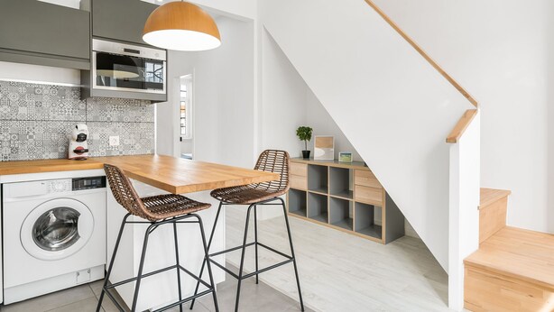 Una cocina moderna con lavadora integrada, dos taburetes y una escalera de madera.